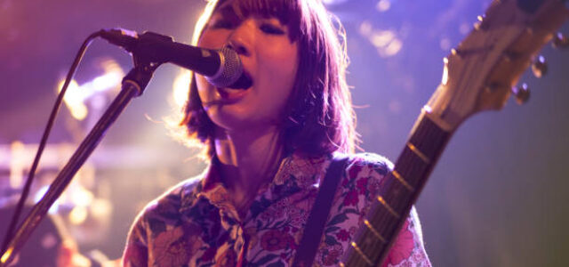 A young Japanese woman is playing the guitar during a live band event.